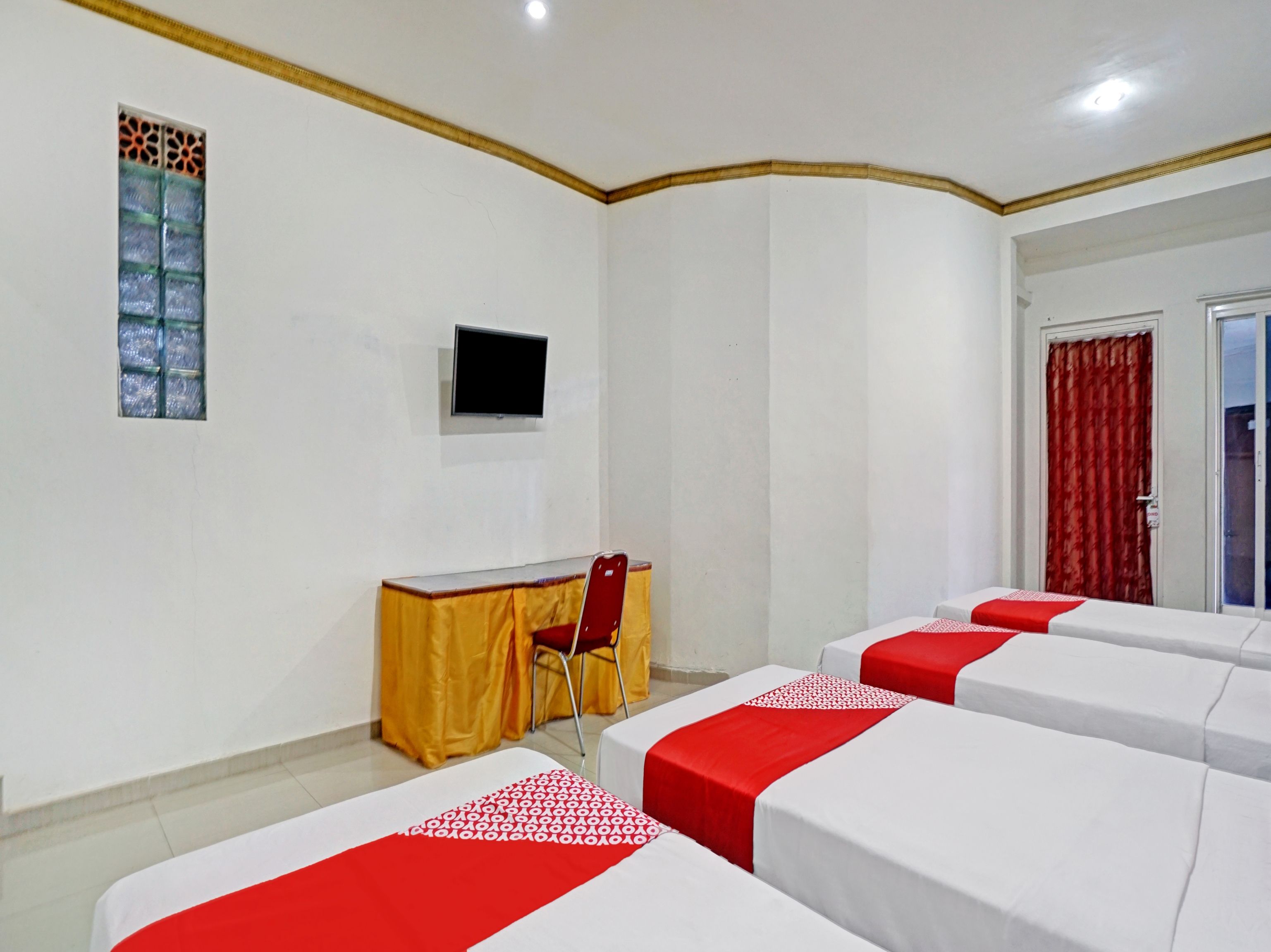 A hotel room with a bed, a desk, a chair, a TV, and a door.