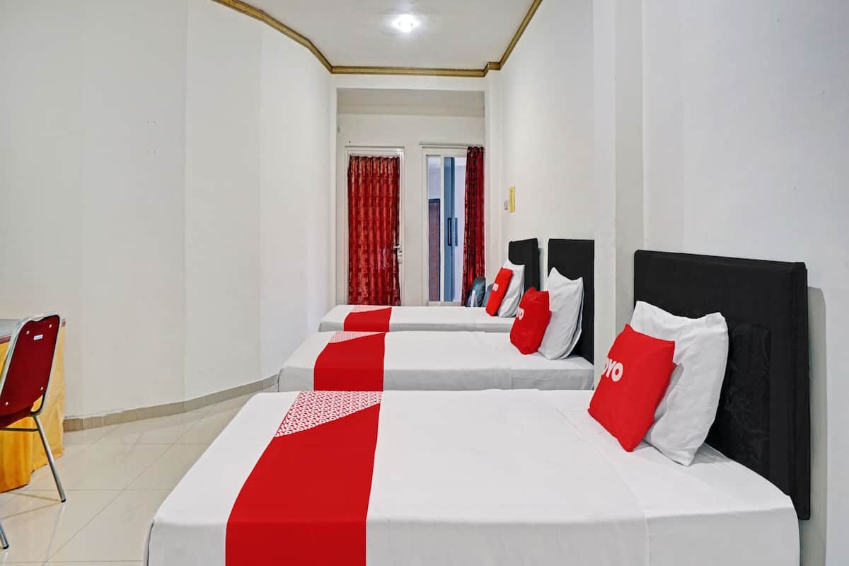 Une chambre d’hôtel avec deux lits, une literie rouge et blanche, un fauteuil rouge et une porte donnant sur une autre pièce.