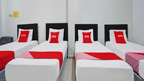 Une chambre d’hôtel avec quatre lits simples, chacun doté d’une tête de lit noire et d’un oreiller rouge et blanc arborant la marque « OYO ».