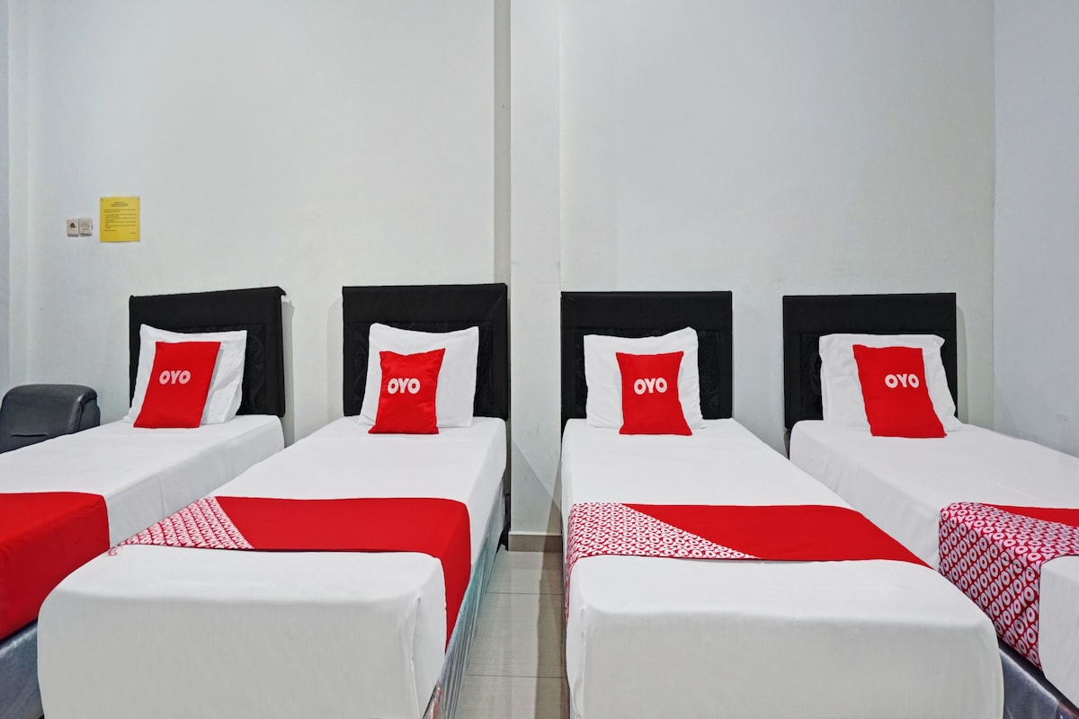 Une chambre d’hôtel avec quatre lits simples, chacun doté d’une tête de lit noire et d’un oreiller rouge et blanc arborant la marque « OYO ».