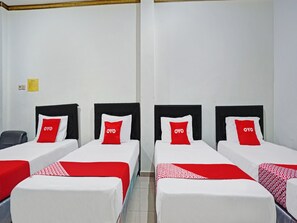 A hotel room with four single beds, each with a black headboard and a red and white pillow with 'OYO' branding. - OYO 90028 Hotel Victory (Batu)