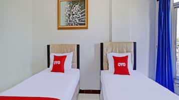 Two single beds with headboards, a framed artwork on the wall, and a window with blue curtains.