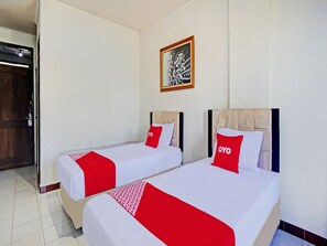 A hotel room with two beds, each with a red and white bedspread and matching pillows. There is a framed artwork on the wall above the beds.