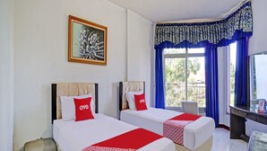 Une chambre d’hôtel avec deux lits, un bureau, une chaise, une fenêtre avec des rideaux bleus et un tableau au mur.