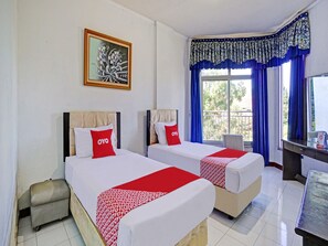 A hotel room with two beds, a desk, a chair, a window with blue curtains, and a painting on the wall. - OYO 90028 Hotel Victory (Batu)