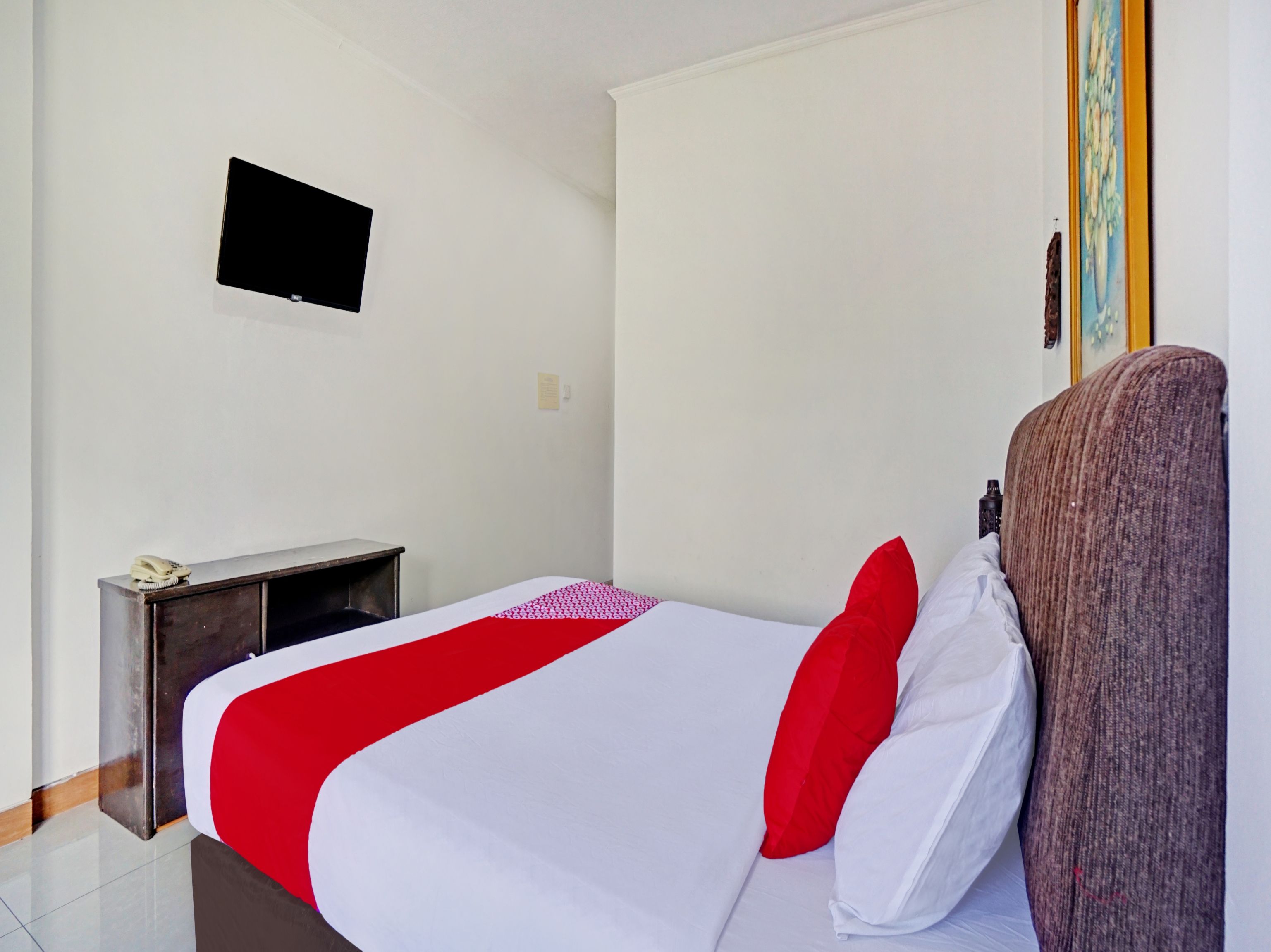 A hotel room with a bed, a desk, a chair, a television, and a painting on the wall.