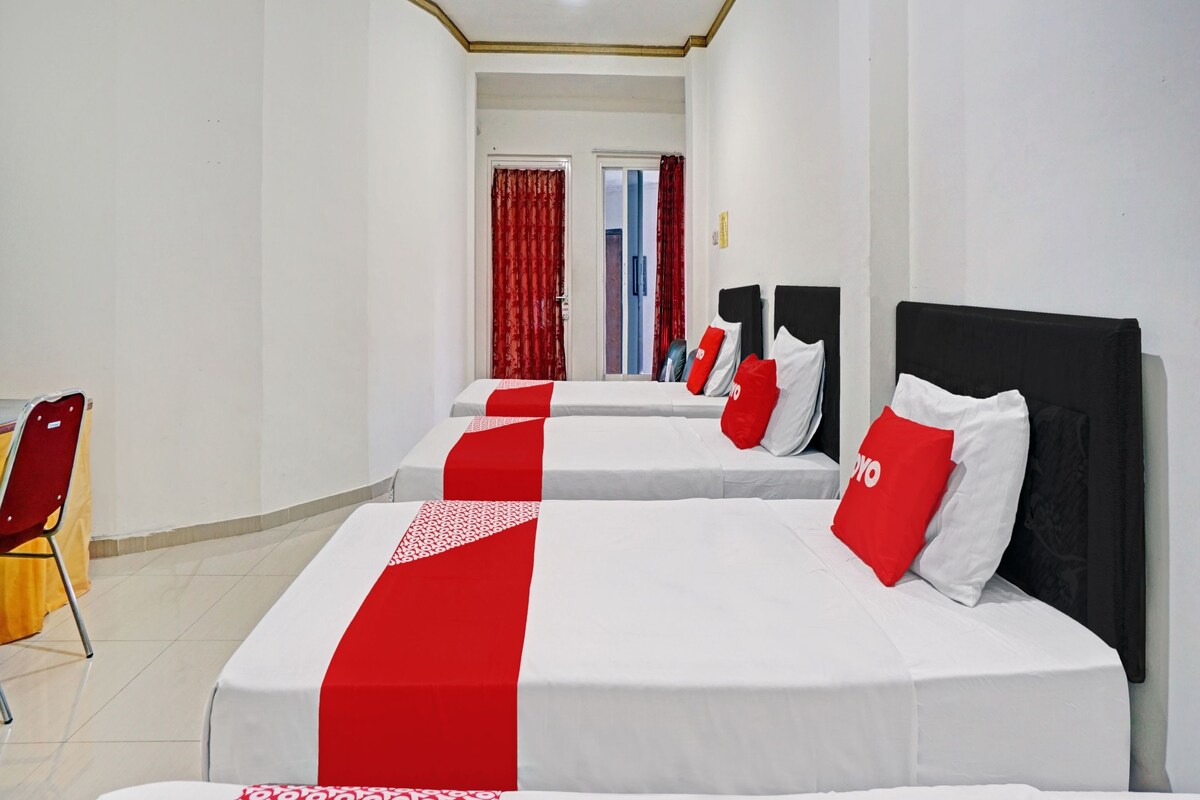 Ein Hotelzimmer mit zwei Betten, roter und weißer Bettwäsche, einem roten Sessel und einer Tür zu einem weiteren Raum.
