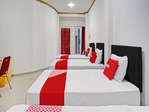 Quarto de hotel com duas camas, roupa de cama vermelha e branca, uma cadeira vermelha e uma porta que dá para outro quarto.