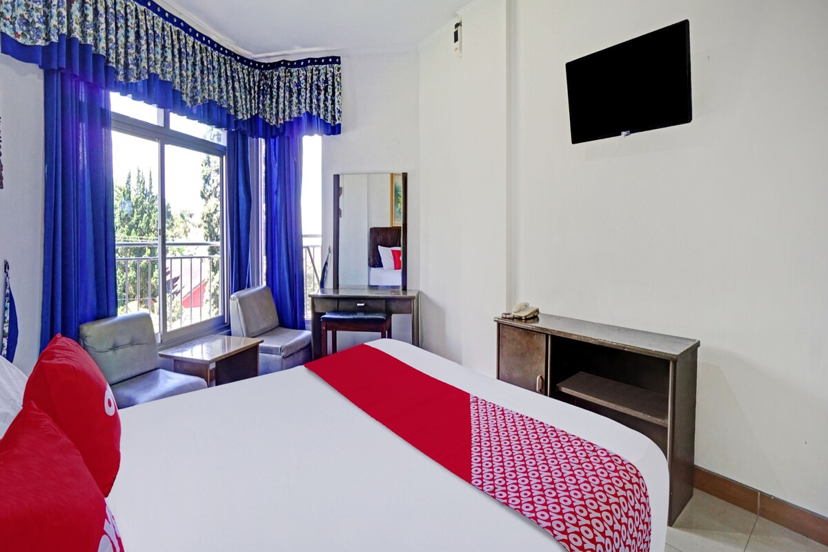 Una camera d'albergo con un letto, una scrivania, una sedia, una TV e un balcone con tende blu.