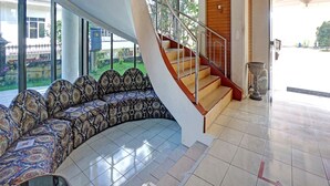 Ein gebogenes Sofa mit gemusterten Bezügen, eine Treppe mit Metallgeländern und ein gefliestes Parkett.