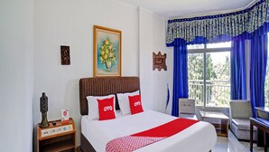 Ein Hotelzimmer mit Bett, Nachttisch, Stuhl, Tisch und einem Balkon mit blauen Vorhängen.
