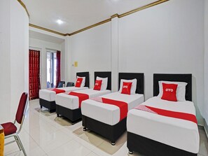 A hotel room with four beds, each with a red and white bedspread and pillows, and a red chair. - OYO 90028 Hotel Victory (Batu)