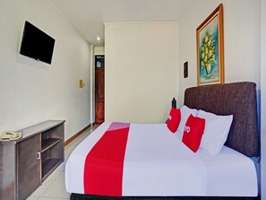Une chambre d’hôtel avec un lit, un téléviseur fixé au mur, un tableau et une porte en bois.