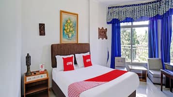 A hotel room with a bed, a nightstand, a chair, a table, and a balcony with blue curtains.