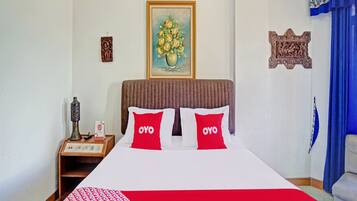 A hotel room with a bed, a nightstand, a decorative vase, a framed painting, and a blue curtain.