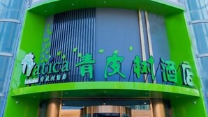 Un hotel con una fachada destacada en tonos verde y azul, que presenta una amplia sección de ventanales y un toldo verde con el nombre del hotel.