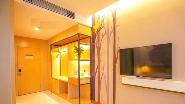Habitación de hotel con cama, televisor montado en la pared, una pequeña mesa de trabajo con una planta y una puerta con un cartel.