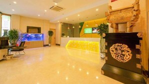 Un vestíbulo de hotel con mostrador de recepción, zona de estar y elementos decorativos, incluyendo una pantalla grande y arte tradicional.