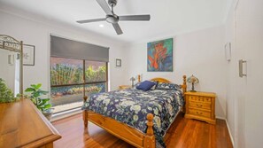 Relax in this serene bedroom with a large bed, ceiling fan, and garden view.