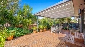 Enjoy dining or socializing in this serene outdoor space surrounded by lush greenery and a partially enclosed canopy.