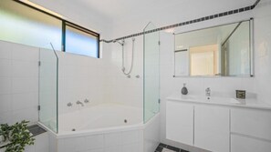 Relax in a spacious bathroom with a bathtub, glass-enclosed shower, and large mirror.