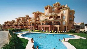 Un hotel con una amplia piscina rodeada de césped cuidado y varios balcones.