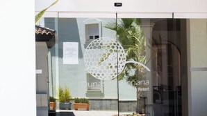 Una puerta de cristal con un adorno metálico, un cartel con información de contacto y el nombre 'Dunas de la Bonana Golf & Resort' a la vista.