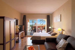 Habitación de hotel con cama, sofá, televisión, escritorio con lámpara y vista al exterior.