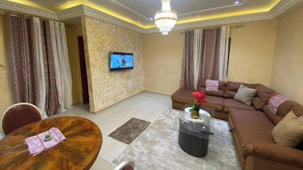 Ein Wohnzimmer mit einer Couch, einem Couchtisch, einem an der Wand befestigten Fernseher und einer Pendelleuchte.