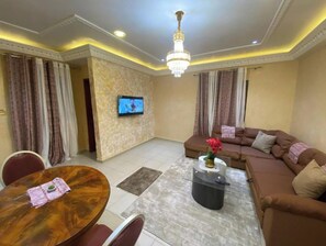 Un salon comprenant un canapé, une table basse, un téléviseur fixé au mur et un lustre.