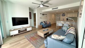 Ein modernes Wohnzimmer mit Flachbildfernseher, einer Couch, einem Couchtisch und einem Deckenventilator.