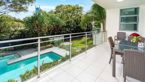 Ein Balkon mit Glasgeländer, der einen Pool und üppiges Grün blickt.