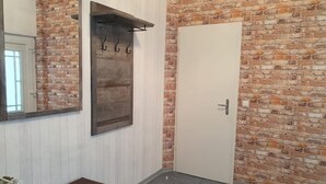 A bathroom with a brick wall, a white door, a mirror, and a bench. - Hübsches Zimmer mit Eigenem Bad und Kochecke, Gute Verkehrsanbindung (Swisttal)
