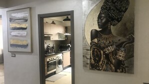 A modern kitchen with stainless steel appliances, a washing machine, and a dining area with a large painting. - Appartement 105m2 Haut Standing Quartier du Parc Proche Plage (Mohammédia)