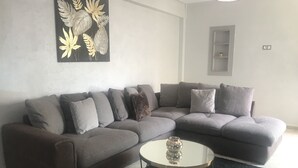 A modern living room with a grey sectional sofa, a round glass coffee table, and a black rug. - Appartement 105m2 Haut Standing Quartier du Parc Proche Plage (Mohammédia)