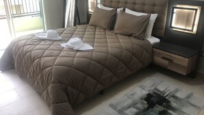 A bed with a brown quilt, two white hats, a nightstand, and a patterned rug. - Appartement 105m2 Haut Standing Quartier du Parc Proche Plage (Mohammédia)