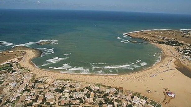 An aerial view of a coastal area with a beach, ocean, and adjacent residential buildings. - Appartement 105m2 Haut Standing Quartier du Parc Proche Plage (Mohammédia)