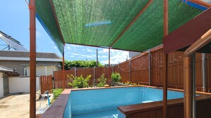 Una piscina en el patio trasero con una terraza de madera y un toldo verde.