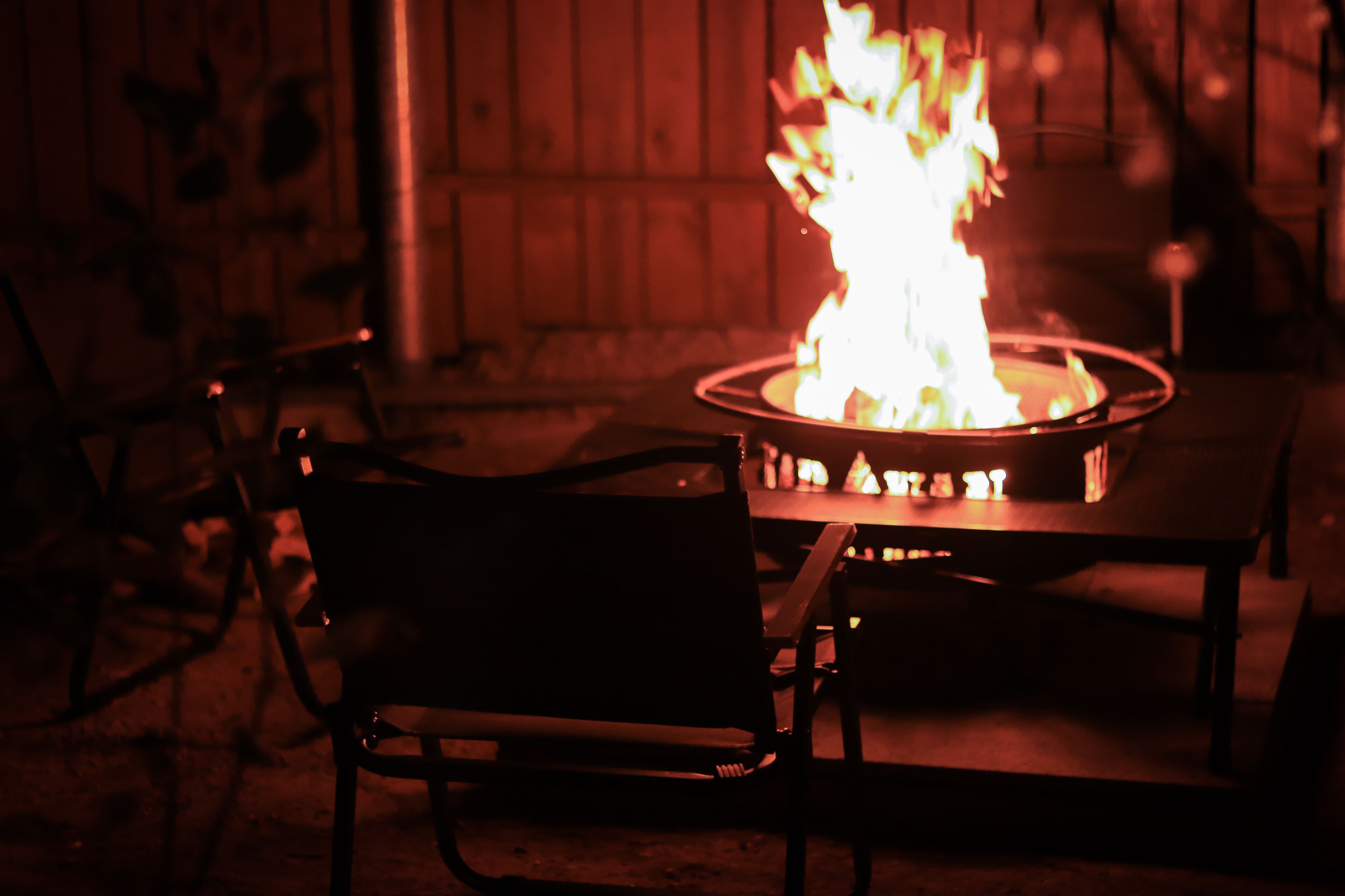 A fire pit with flames, surrounded by metal chairs.
