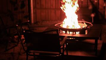 A fire pit with flames, surrounded by metal chairs.