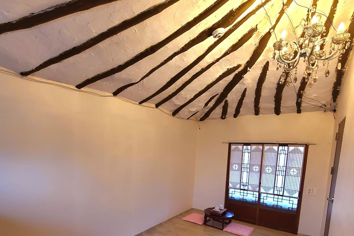 Une pièce avec un plafond en pente, un lustre, une fenêtre avec des barreaux et un lit recouvert d’une courtepointe matelassée.