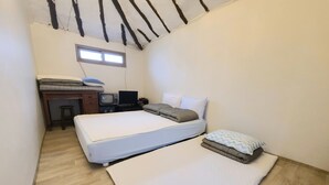 Una habitación pequeña y funcional con dos camas, un escritorio con televisor y un ventanal que deja entrar luz natural.