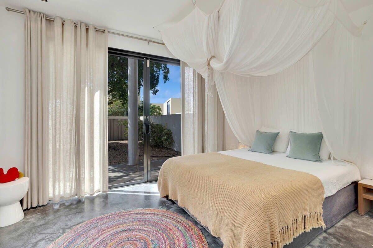 A bedroom with a bed, curtains, a window, and a view of the outdoors.