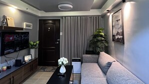 Un salon moderne avec un canapé gris, une table basse noire, un téléviseur fixé au mur et une plante en pot.