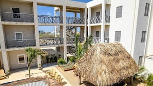 Un immeuble à plusieurs étages doté de balcons, une structure à toit de chaume et des espaces de repos en plein air.