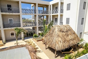 Un immeuble à plusieurs étages doté de balcons, une structure à toit de chaume et des espaces de repos en plein air.