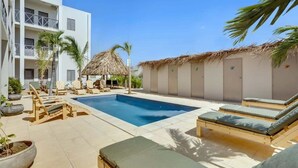 Un espace piscine avec des chaises longues et une structure dotée d’un toit de chaume.