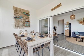 Un espace repas avec une table blanche, des chaises en osier et une cloison en verre.