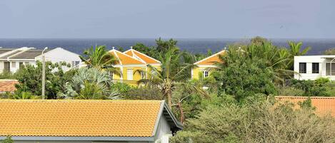 A coastal residential area with houses featuring orange tiled roofs and white walls, surrounded by lush greenery.