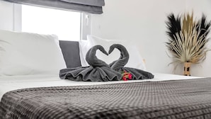 Une chambre d’hôtel avec un lit soigneusement fait, une décoration en forme de cœur réalisée avec des serviettes et une plante décorative.